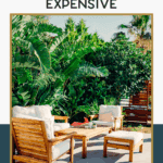 Wooden outdoor furniture with white cushions is arranged on a patio surrounded by lush green plants and trees, creating a stylish and inviting seating area.