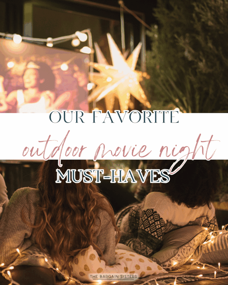 People sit on blankets with pillows, watching an outdoor movie at night. String lights, a star-shaped lantern, and a large screen showing a movie create a cozy atmosphere. Text reads, "Our Favorite Outdoor Movie Night Must-Haves.