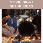 Three people lying on blankets and pillows outside, watching a movie projected on a screen. String lights and outdoor planters create a cozy atmosphere. Text reads: "Easy Outdoor Movie Night Setup Ideas. Read more. thebargainsisters.com.