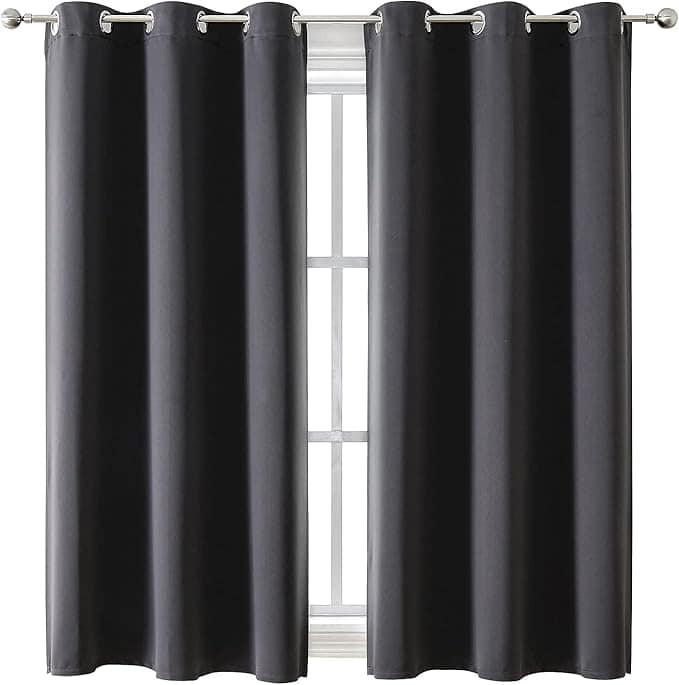 A pair of dark blackout curtains hanging on a silver curtain rod, partially covering a window with multiple glass panes. Featuring metal grommets for easy sliding, these curtains are perfect for Monday Deals shoppers.