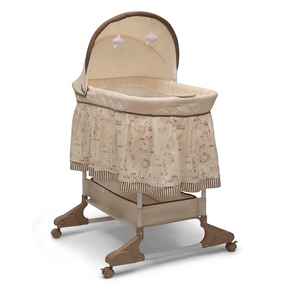 A beige baby bassinet with a fabric canopy, two hanging plush stars, a patterned skirt with stripes and animal designs, and a lower storage shelf on wheeled legs—perfect for your nursery and available now in our Thursday Deals.