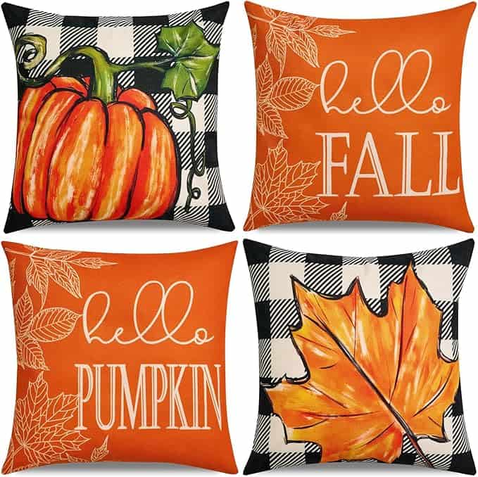 Four decorative throw pillows: one with a pumpkin on a black-and-white checkered background, one with "hello FALL" and leaf outlines, one with "hello PUMPKIN," and one with a large fall leaf on a checkered background—perfect for Friday Deals.