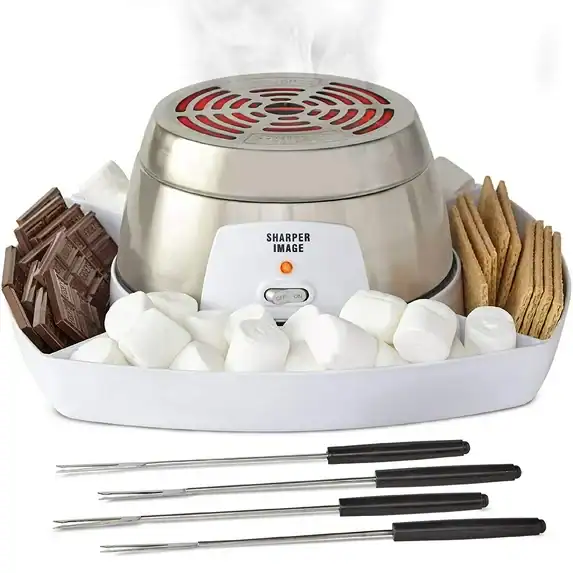 A tabletop s'mores maker with a metal heating element in the center, surrounded by chocolate bars, graham crackers, and marshmallows—perfect for cozy nights. Four roasting sticks sit in front, making it a sweet pick for Tuesday Deals.