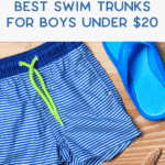 Blue and white striped swim trunks with a neon green drawstring next to blue flip-flops, seashells, and a starfish on a wooden surface. Text reads: “Best Swim Trunks for Boys Under $20.”.