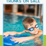 A young boy wearing blue goggles smiles while swimming in a pool, holding a blue kickboard. Text above reads, "Our favorite boys swim trunks on sale." Website "thebargainsisters.com" is at the bottom.