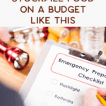 A clipboard with an emergency prep checklist is held in the foreground; a flashlight, batteries, and water bottles are listed. In the background, supplies like a flashlight and canned food are visible. Text reads: "Stockpile food on a budget like this.
