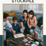 A family of four sits together in a living room, looking at a food stockpile plan on the table surrounded by canned goods, water bottles, and emergency supplies. Text above reads, “How to Start a Budget Food Stockpile.”.