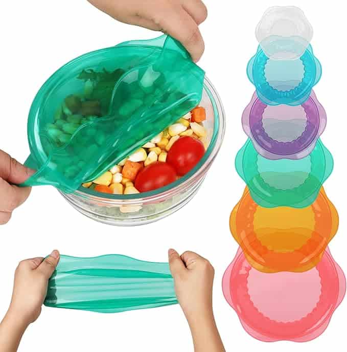 A person stretches a green silicone food cover over a glass bowl filled with vegetables. Next to the bowl, six colorful silicone covers in various sizes are stacked—perfect for keeping food fresh and saving big with Friday Deals.