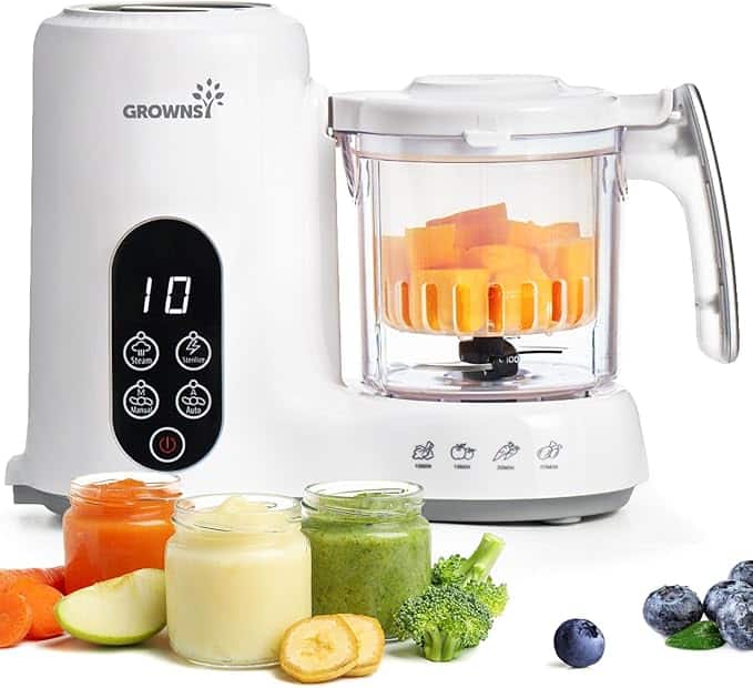 A white baby food maker with a digital display and control buttons is blending orange vegetables. In front are jars of pureed carrot, banana, broccoli, and assorted fresh fruits—perfect for healthy meals or scoring Friday Deals.