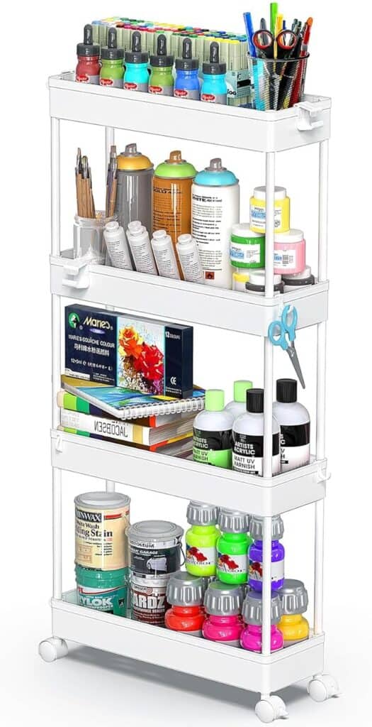 A white three-tier rolling cart holds various art supplies—paint bottles, brushes, colored pencils, spray cans, markers, scissors, and sketch pads—all neatly organized on each shelf. Perfect for creative spaces and Friday Deals shopping sprees.