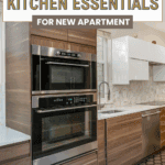Modern kitchen with wood cabinets, stainless steel double oven, white upper cabinets, and a marble backsplash. Text reads, "Budget-Friendly Kitchen Essentials for New Apartment.