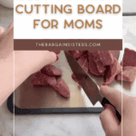 A person slices raw meat on a metallic cutting board in a kitchen. Text overlay reads: "Best titanium cutting board for moms. thebargainsisters.com". Sliced cucumbers and apples are visible in the background.