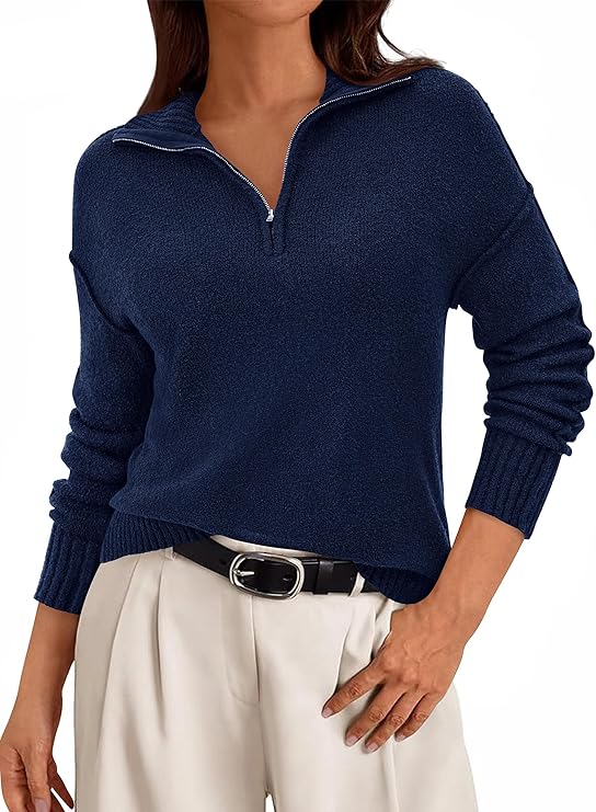 A person wearing a navy blue zip-collar sweater with long sleeves and beige high-waisted pants, accessorized with a black belt, stands with one hand on their hip—perfect inspiration for your Thursday Deals shopping.