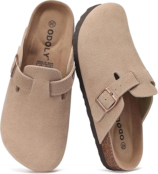A pair of beige suede clogs with adjustable side buckles and cork soles, displayed with one shoe upright and the other lying on its side. The brand "ODOLY" is visible on the insole—perfect for snagging during Friday Deals.