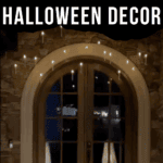 A stone wall with a large arched wooden door is decorated with floating candles hanging from the ceiling, and two ghost decorations standing on either side of the door. Text reads: “Spooky Floating Candles Halloween Decor.”.
