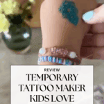A child's hand with a sparkly blue temporary tattoo on the back, wearing colorful beaded bracelets, with flowers and a vase blurred in the background. Text reads, "Review: Temporary Tattoo Maker Kids Love.
