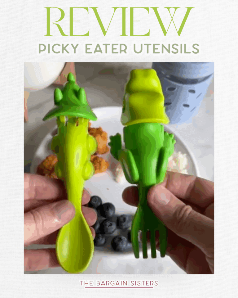 Two hands hold playful green utensils shaped like alligators, one a spoon and the other a fork. Food, including blueberries, rice, and chicken, is visible in the background—next to an air conditioner cover. Text reads: "Review: Picky Eater Utensils.