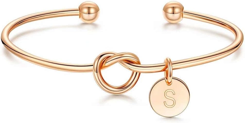 A gold cuff bracelet with a knot design in the center, open ends with round beads, and a small round charm engraved with the letter "S" hanging from the knot—perfect for treating yourself during Thursday Deals.