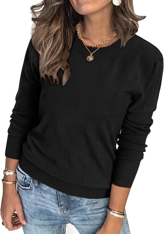 Woman wearing a black long-sleeve sweater with a subtle checkered pattern, light blue jeans, layered gold necklaces, hoop earrings, and bracelets. Her brown wavy hair is worn down.