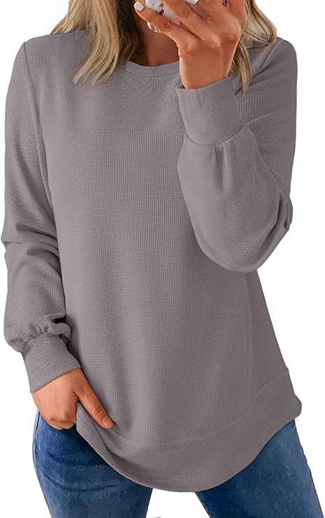 A person wearing a long-sleeved, textured gray sweater paired with blue jeans, holding a phone in one hand and resting the other in their pocket—ready to check out this week's Friday Deals. Their face is not visible.