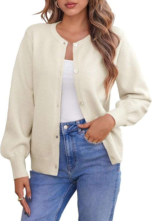 A woman wearing a cream-colored button-up cardigan over a white top and blue jeans, with long wavy hair and minimal jewelry.