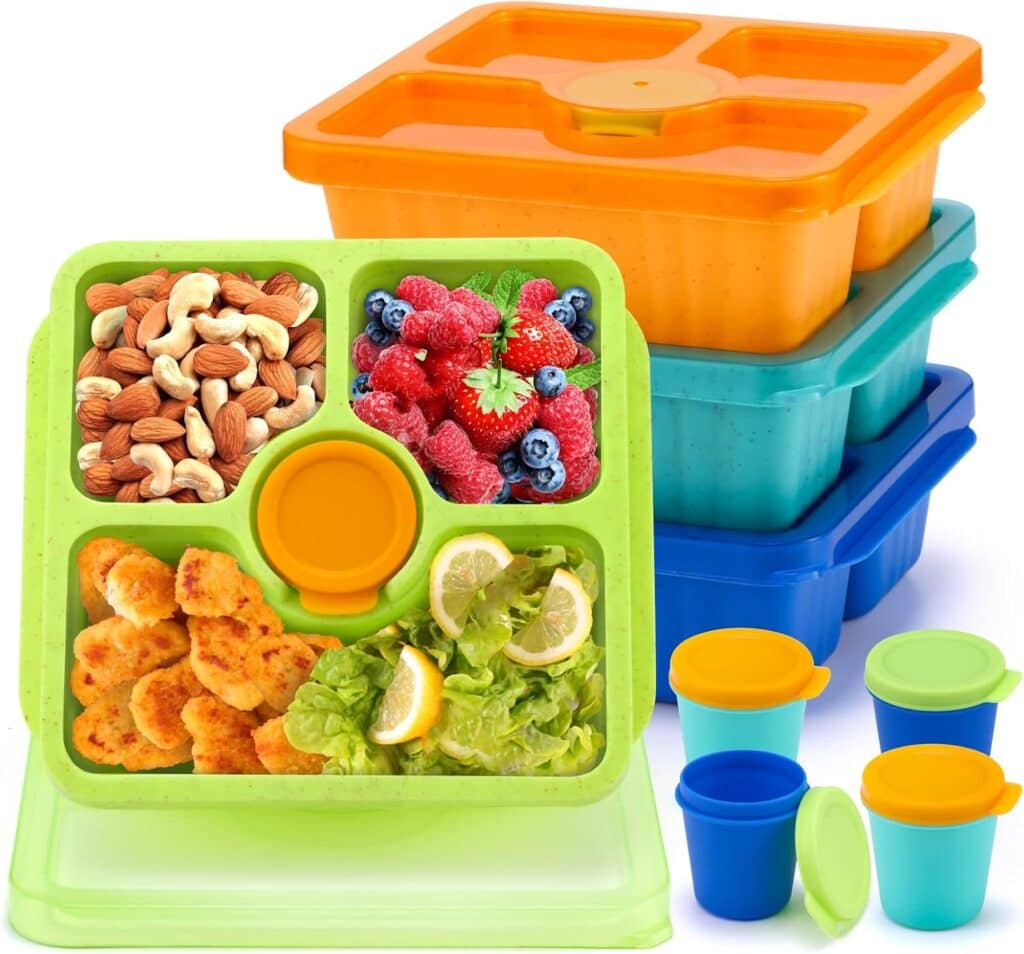 A green segmented Bento Snack Box holds nuts, mixed berries, chicken nuggets, and salad with lemon slices. Behind it are stacked orange, blue, and green snack boxes with lids and four small colorful containers with lids.
