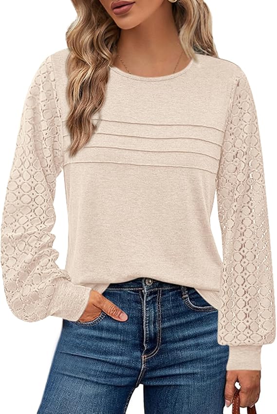 A woman wearing a beige long-sleeve top with lace-patterned sleeves and blue jeans, with one hand in her pocket. Her blonde hair is styled in loose waves. The image is cropped at the shoulders and mid-thigh.