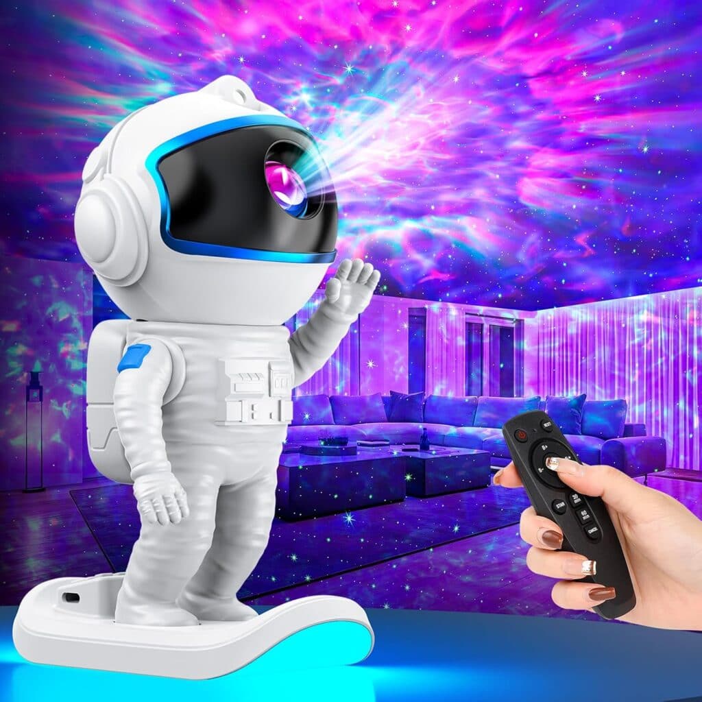 A hand holds a remote control, aiming at a small astronaut-shaped projector that displays colorful, swirling purple and blue lights onto the ceiling and walls of a modern living room.