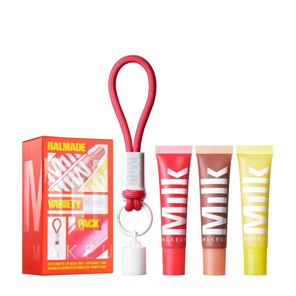 A red and yellow box labeled "BALMADE VARIETY PACK" sits beside three colorful tubes labeled "MILK MAKEUP" in pink, orange, and yellow, with a white keychain holder featuring a red loop.