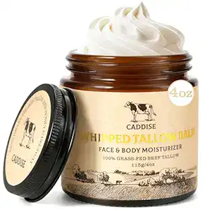 An open jar of Caddise Whipped Tallow Balm, labeled as a face and body moisturizer made with 100% grass-fed beef tallow. The jar is brown with a cream-colored label and lid, showing 4 oz size. The balm is whipped and creamy.