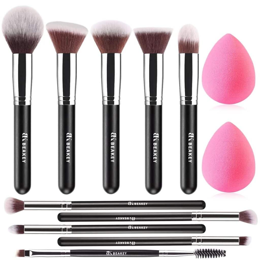 A set of ten black-handled makeup brushes with silver ferrules, two pink makeup sponges, and five dual-ended eye brushes, all arranged neatly on a white background.