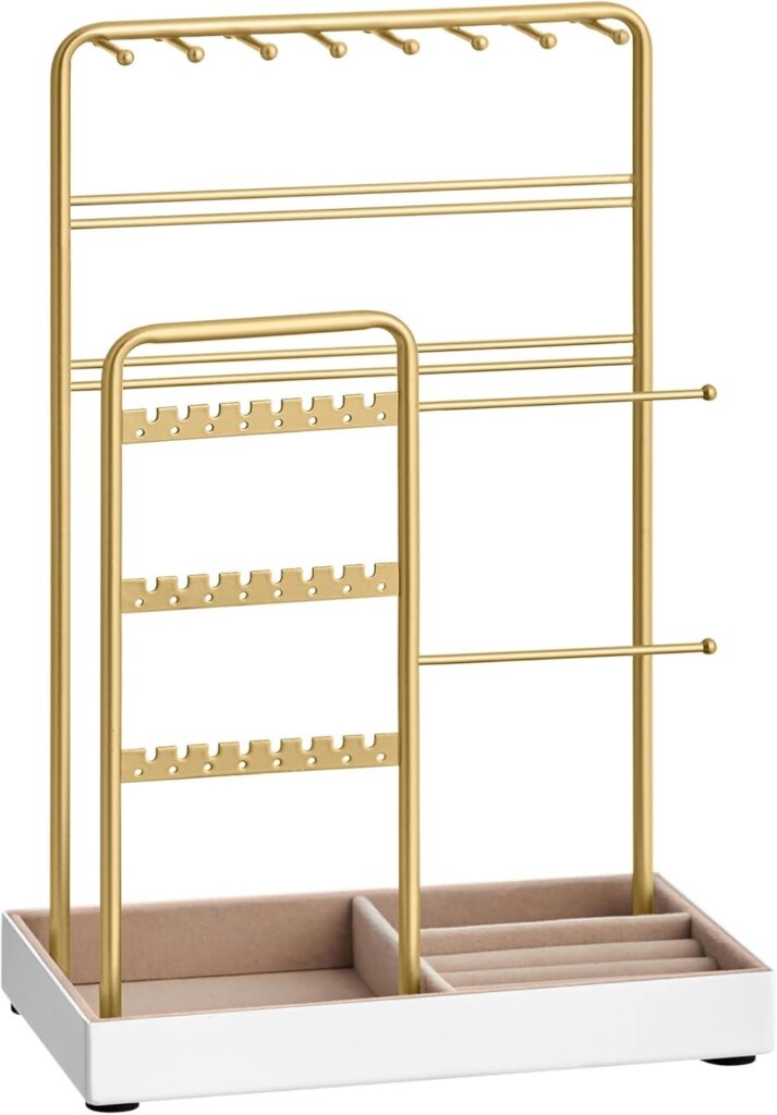 A gold metal jewelry organizer with multiple bars and hooks for hanging necklaces, bracelets, and earrings, set on a rectangular white tray with divided sections for rings and small items.