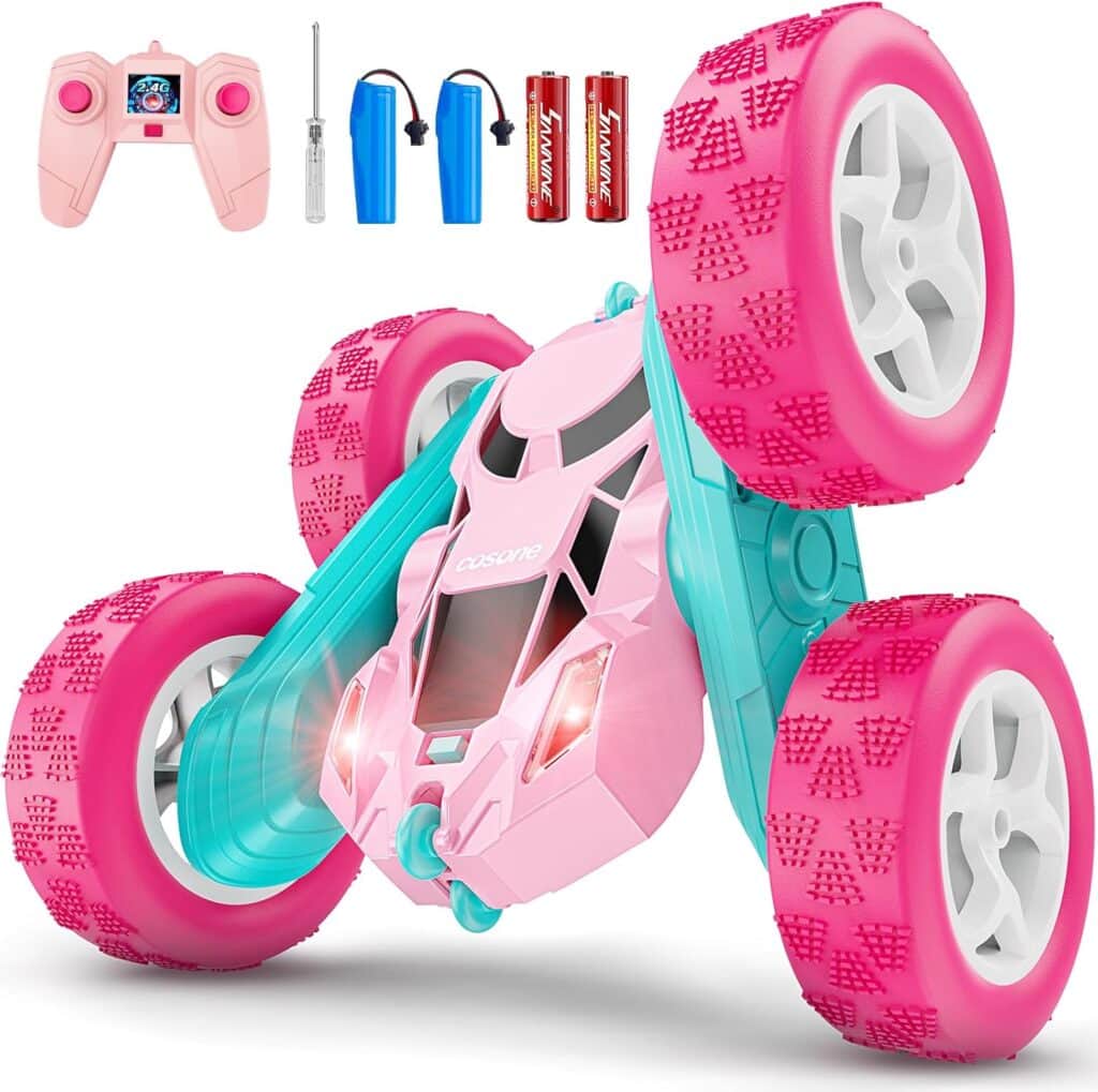 A pink and blue remote control stunt car with large tires, shown with a pink controller, two blue batteries, a small screwdriver, and two AA batteries. The car features headlights and a durable, flip-capable design.