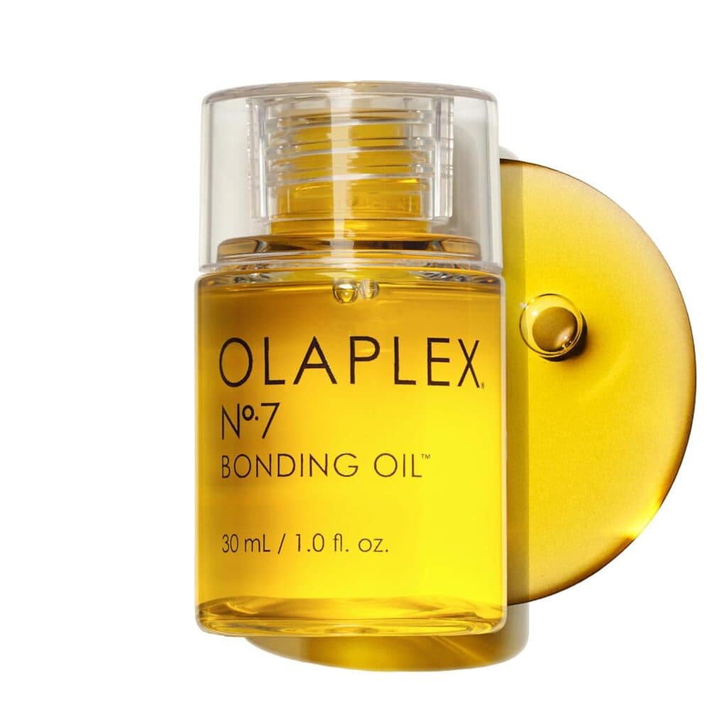 A clear bottle of Olaplex No. 7 Bonding Oil, a Premium Beauty essential, with a transparent cap and golden yellow oil, is displayed against a white background accented by a circular yellow reflection.
