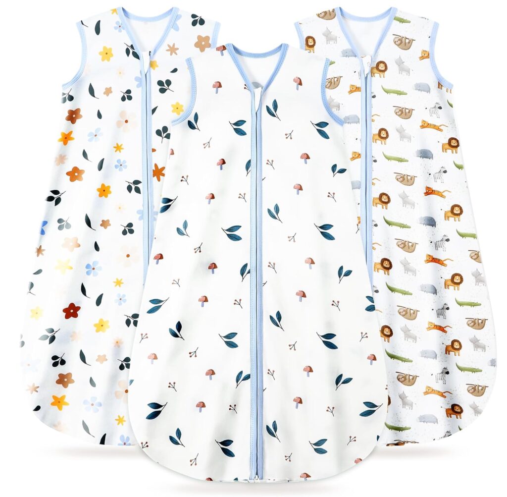 Three sleeveless baby sleep sacks with blue trim and zipper fronts; one has a floral pattern, one has mushrooms and leaves, and one features animals like lions, crocodiles, and sheep.