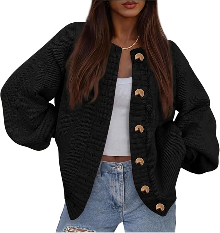 A woman wearing a black oversized cardigan with large gold buttons over a white cropped tank top and light blue jeans, standing with her hands in her pockets.