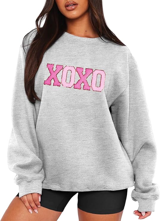 A woman wearing a gray sweatshirt with "XOXO" in large pink letters across the chest, paired with black shorts.