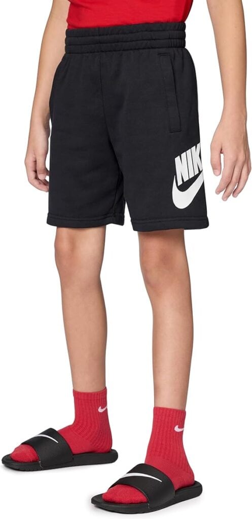 A person wearing black Nike shorts, a red shirt, red Nike socks, and black Nike slide sandals stands with their arms relaxed at their sides.
