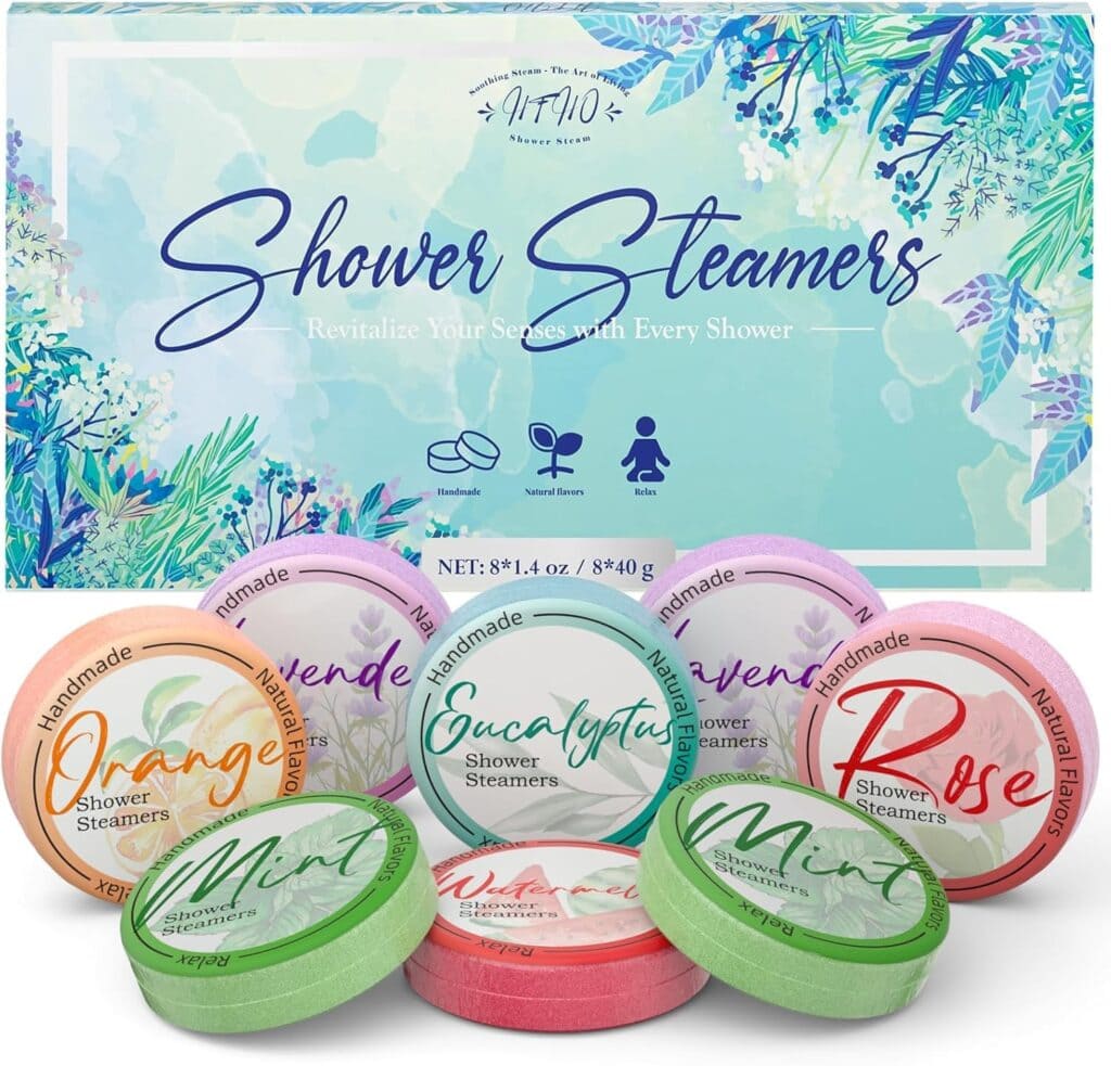 Box of "Shower Steamers" with floral design, featuring seven colorful round tablets labeled with scents: Orange, Eucalyptus, Mint, and Rose. The packaging highlights they are handmade, natural, and suitable for all genders.