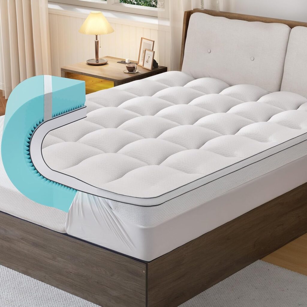 A neatly made bed with a white, quilted mattress topper partially lifted to show its thickness and soft texture, in a cozy bedroom with a lamp, nightstand, and window in the background.
