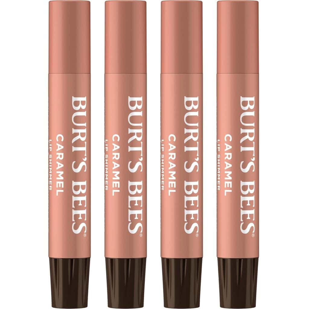 Four Burt's Bees Caramel Lip Shimmer tubes are standing upright in a row, with rose-gold colored bodies and dark brown caps. The product name and brand are printed vertically in white text.