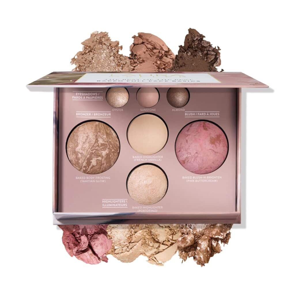 An open makeup palette displays various powders including eyeshadows, bronzer, highlighter, and blush, with crushed powder colors scattered decoratively around the palette on a white background.
