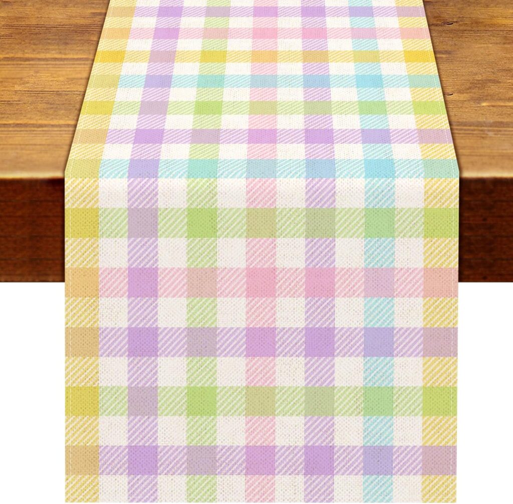 A pastel-colored checkered table runner with a plaid pattern in pink, yellow, green, blue, and purple, displayed on a wooden table.