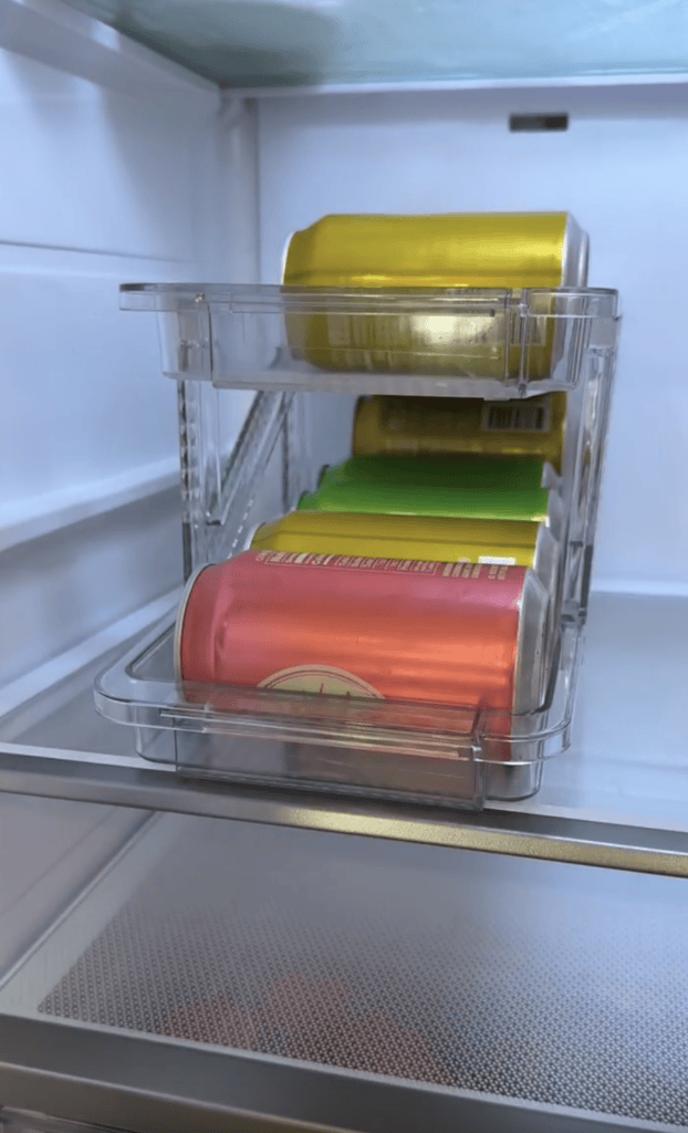 Several colorful soda cans, including pink, yellow, and green, are neatly stacked in clear plastic organizers inside a refrigerator—perfect for moms who love celebrating with a reusable cake candle holder on hand.