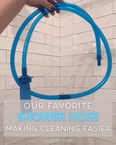 A hand holds up a blue shower hose in a white tiled shower. Text at the bottom reads: “Our favorite shower hose making cleaning easier—for busy moms. The Bargain Sisters.”.