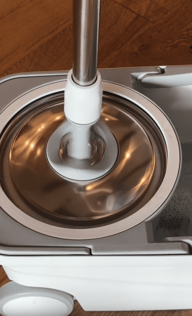 A close-up of a mop head being spun dry in a stainless steel spin basket of a white mop bucket, perfect for moms who value spotless wooden flooring in their homes.