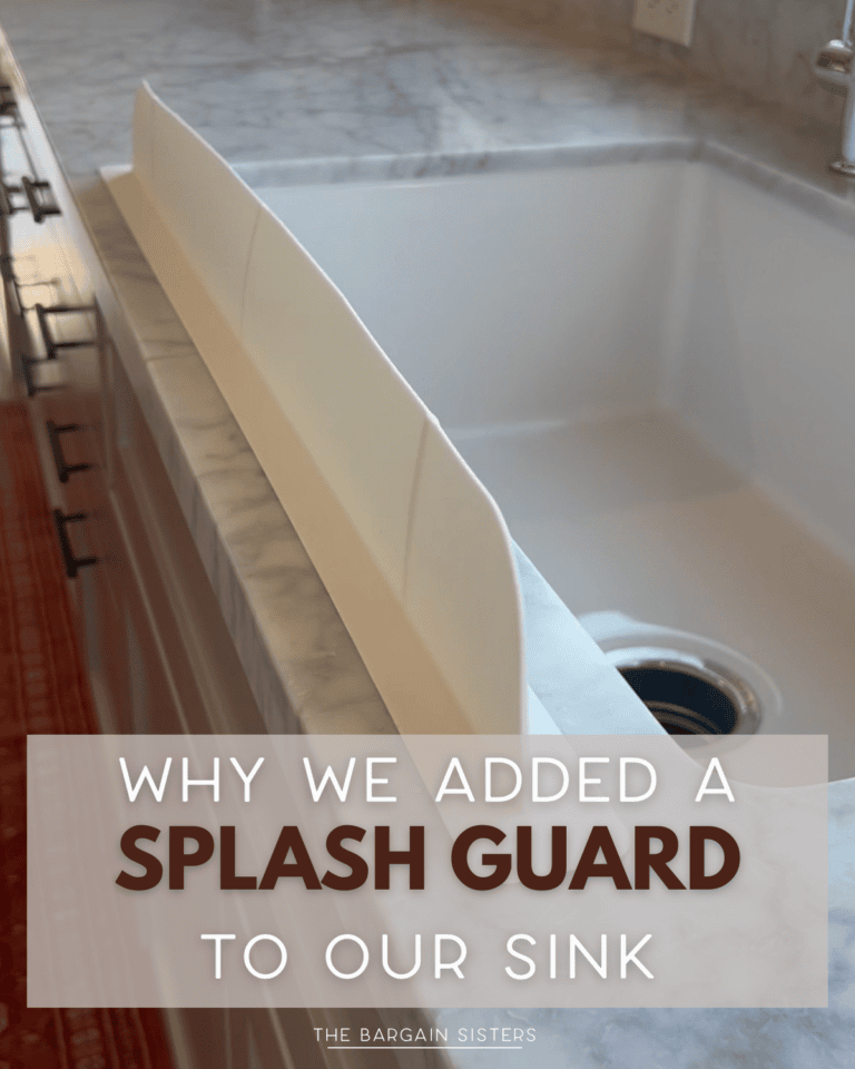 A marble kitchen countertop with a white sink features a tall, white splash guard along the edge—perfect for busy moms. Overlaid text reads, "Why we added a splash guard to our sink.