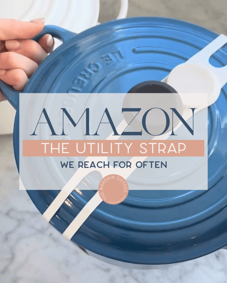 A hand holds a blue Le Creuset pot lid with a white utility strap across it—perfect for busy moms. Overlaid text reads: “AMAZON THE UTILITY STRAP WE REACH FOR OFTEN.” The background is a marble countertop.