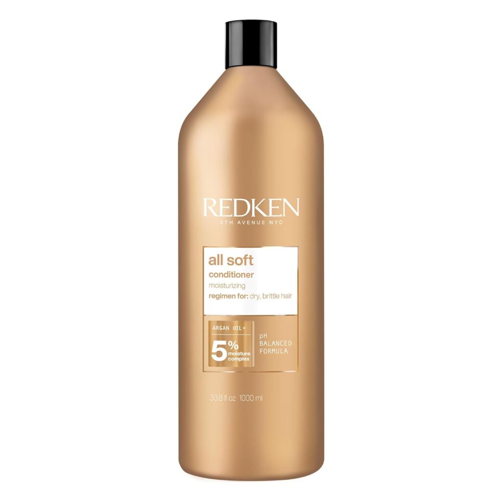 A large gold bottle of Redken All Soft conditioner with a black cap, featuring white and brown text highlighting its moisturizing formula for dry, brittle hair and containing argan oil. The bottle size is 1000 ml.