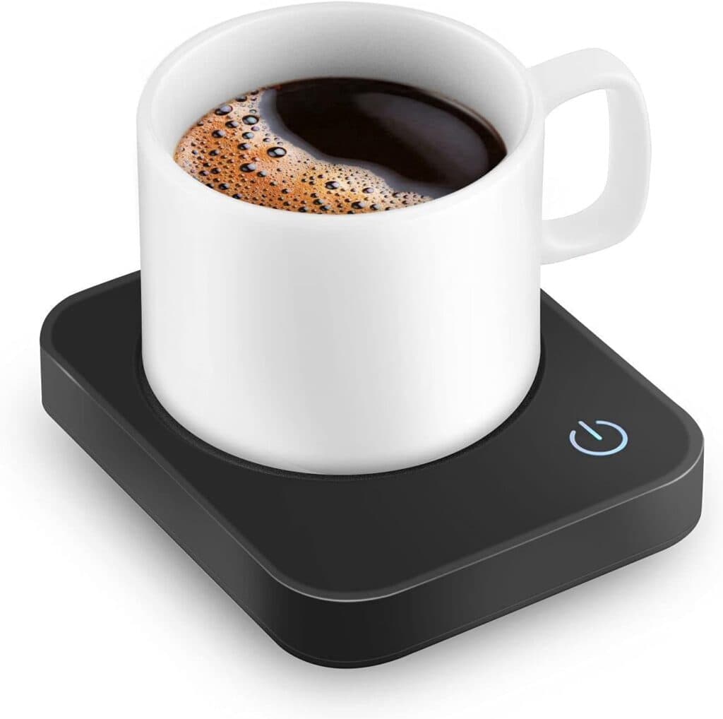 A white coffee mug filled with black coffee sits on a black electric mug warmer with a glowing power button.